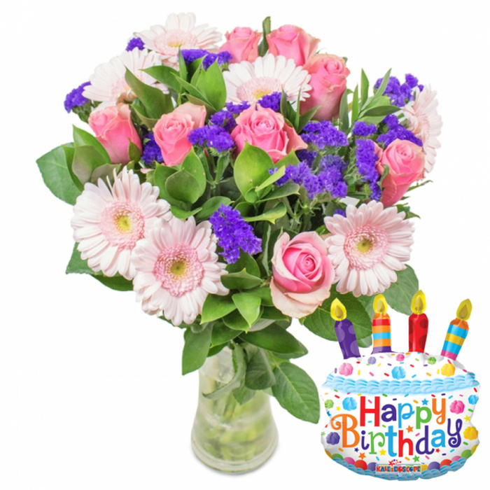 Set against a simple white backdrop, this celebratory composition combines classic floristry with a fun party accent-a clear glass vase overflowing with fresh blooms beside a cake-shaped Mylar balloon. The arrangement centers on a generous collection of soft pink roses, their petals layered and plush, shading from a pale blush at the outer edges to a deeper pink toward their hearts. Interspersed among them are pale pink Gerbera daisies, their wide, petalled faces and pale yellow-green centers offering a cheerful counterpoint to the roses' softness. Piercing through the pastel field are abundant clusters of vivid purple filler flowers-statice or limonium-which add crisp texture and a jewel-like pop of color that lifts the bouquet's overall palette. Rich, glossy green foliage frames each bloom, providing structural depth and a fresh, leafy backdrop; the slender green stems are visible through clean water in the vase, underscoring the flowers' recent harvest. To the right-hand side, a festive, white cake-shaped balloon adds narrative: a blue wavy 'icing' border, a spray of colorful sprinkles in red, yellow, blue and green, and four small candles-purple, red, orange and blue-topped with yellow flame motifs. The words Happy Birthday appear in lively, multicoloured typography across the balloon, while the small brand name KALEIDOSCOPE rests at its base. The overall mood is bright yet tender, an ideal birthday surprise for someone local to Mill Hill Park or a thoughtful pick-up for a celebration on Bittacy Hill-balanced, fragrant, and made to arrive fresh and ready to delight.