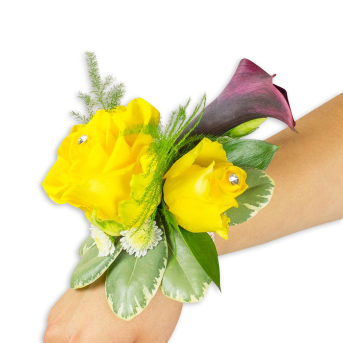 A compact, meticulously arranged wrist corsage rests on a light-to-medium forearm against a pure white studio field, the kind of detailed image that highlights both craft and colour. Dominating the design are two vivid yellow roses - the left blossom fully unfurled and generous, the right slightly smaller and more cupped - with each rose crowned by a discreet clear crystal set near its heart, throwing off tiny pinpoints of light. Behind and slightly above these sun-bright flowers, a single deep burgundy-to-plum calla lily unfurls in a smooth, trumpet shape, its dark, glossy surface creating a sophisticated foil to the warm yellow. The floral matrix is enriched with fine asparagus fern that gives an airy, filigreed texture, while broad variegated leaves with pale edges provide structural weight and cool, waxy contrast. Small, white spray flowers are tucked into hollows between leaves and petals, lending the corsage a fuller, garden-like silhouette.
Worn diagonally across the wrist from bottom-left to mid-right in the frame, the piece shows how mobility and comfort were considered in its fastening. The overall impression is bright, confident and poised - a celebratory accent suited to a Mill Hill wedding, a prom night departing from Mill Hill Broadway, or a special event near Mill Hill Park - with a soft floral scent and a tactile mix of satin petals, crisp foliage and delicate fern.