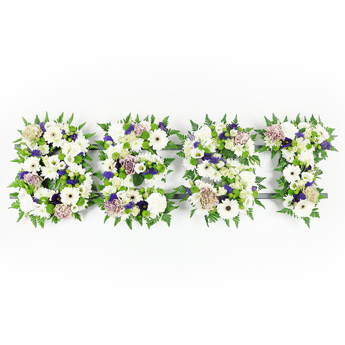 An elegant, horizontal floral display spells the word BEST in bold, uppercase letters, each character formed from a dense, harmonious blend of white blooms, lavender accents, and lush greenery. The composition is dominated by large, pristine white gerbera daisies with their dark centres, full white carnations, and soft lisianthus, layered to create a tranquil yet textured surface. Scattered among these are mauve and lavender roses, together with small clusters of deeper purple filler blossoms that introduce a gentle solemnity and depth of tone. Pops of lime-green button chrysanthemums sit low within the clusters, bringing clarity and visual contrast against the creams and lavenders. Fine, feathery fern fronds trace and frame the edges of every letter, their delicate fronds softening the geometry and giving each character a natural, verdant outline. A dark grey structural base holds the work together, visible in places and giving the floral letters discreet definition on the bright white background. Soft light reveals the varied textures - the satiny rose petals, the papery gerbera faces, the ruffled carnation edges - and suggests the quiet scent of roses and fresh greens. Crafted by Flowers Mill Hill for families across Mill Hill and nearby streets like The Broadway and Bittacy Hill, this type of tribute is chosen for funerals and memorials where a clear, personal message of love and remembrance is needed. The overall impression is one of respectful artistry: a carefully balanced, heartfelt expression that reads as both a farewell and a celebration of a well-loved life.