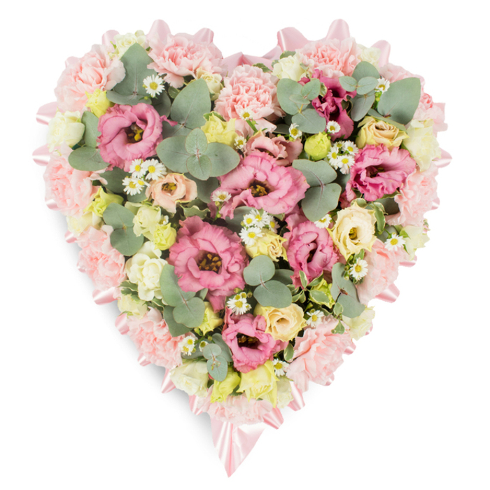 A delicately crafted heart-shaped floral arrangement is set against a clean white background, composed in soft pastels that give it a calm, consoling presence, perfectly suited to a memorial service or funeral in Mill Hill. The outer edge of the heart is built from a dense band of pale pink carnations, their softly frilled petals layering over one another to create a plush, almost pillow-like border. Following this outline, a gentle pink satin ribbon can be seen, its smooth, light-catching surface weaving in and out between the blooms and tying into neat bows that sit with understated elegance at the top curve and lower point of the heart. Within this floral frame, the heart is filled right to the centre with a carefully balanced mix of fresh flowers and foliage. Ruffled pink lisianthus blossoms take pride of place, some open wide with elaborate petals, others still slightly cupped, suggesting life and movement. Around them cluster small creamy and pale yellow spray roses, whose rounded buds bring subtle warmth and softness. Tiny, white daisy-like flowers with golden centres are sprinkled through the design, breaking up the larger shapes and adding a sense of delicacy and light. To complement the flowers, sprigs of eucalyptus, with their distinctive round, silvery-green leaves, are woven between the blooms along with deeper green foliage, giving structure and a soothing, natural contrast. The overall effect is full yet gentle, as though arranged by a local Mill Hill florist familiar with the area's churches and crematoriums, then prepared for respectful delivery. This heart-shaped tribute quietly conveys love, remembrance, and compassion, offering a tender way to say goodbye to someone cherished within the Mill Hill community.