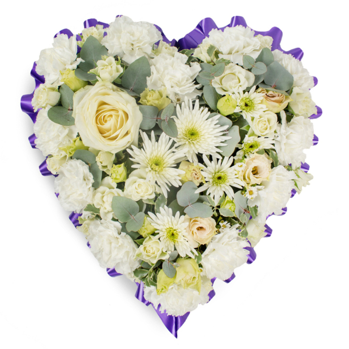A meticulously designed heart-shaped funeral arrangement is displayed against a simple white background, ensuring that every flower and ribbon fold is clearly visible. The heart is lavishly covered in a tapestry of white and cream blossoms, so closely arranged that the surface looks luxuriously padded and complete. At the centre, a single, large creamy white rose is positioned as the emotional focal point, its petals gracefully spiralling outward with a smooth, velvety finish that speaks of pure affection and remembrance. Radiating from this central bloom, an abundance of white carnations sweeps along the curves of the heart, their ruffled petals layered in undulating waves that create a soft, rounded profile. Between them, spidery white chrysanthemums extend their fine, needle-like petals, adding a touch of movement and contemporary flair. Clusters of smaller roses, some in tight buds and others just beginning to open in shades of ivory and the palest lemon, are interspersed with delicate filler flowers that echo the light, airy feeling of springtime walks along the green spaces near Mill Hill's Dollis Brook. Throughout the design, muted blue-green eucalyptus sprigs peek out, their smooth, almost silvery leaves providing gentle contrast in tone and form, as well as a suggestion of natural fragrance. Encapsulating the entire piece is a deep purple, pleated ribbon border, meticulously ruffled to form a scalloped edge that crisply outlines the heart shape and introduces a subtle sense of ceremony and gravitas. This floral heart feels timeless and sincere, the kind of tribute chosen for services in Mill Hill churches or crematoria nearby, offering a visual expression of sympathy, love, and quiet farewell that supports families during moments of loss.