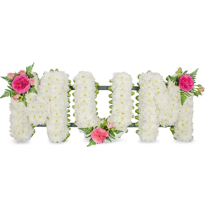 Shown against a pure white backdrop, this floral tribute spells out the word MUM in generous block capitals, the design carefully crafted to offer comfort at a time of loss. The underlying structure is a dark green frame that connects the three letters, giving them support while allowing them to be displayed neatly at a funeral venue in Mill Hill, perhaps near Mill Hill East or along the Ridgeway. Over this frame, the florist has meticulously placed hundreds of white spray chrysanthemums, each tiny bloom nestled so closely that the letters appear completely cushioned in soft petal layers. The chrysanthemums create a uniform, plush texture, with a slightly domed surface that seems almost touchable, like a padded fabric. Their clean white hue symbolises purity and a peaceful farewell, while the even, bright lighting in the image highlights every curl of petal without casting harsh shadows. To personalise the tribute, three harmonising clusters of pink flowers and greenery are arranged with balance and intention. On the top left of the first M, a striking fuchsia garden rose, fully opened, forms the centrepiece of an accent spray, surrounded by smaller blush-pink spray roses and delicate buds. Wisps of fresh green fern weave between the petals, their serrated edges and arching stems adding gentle movement. The U holds a similar grouping at the bottom centre, tucked into its curve like a small posy placed by hand. Completing the composition, the top right of the second M is adorned with an identical cluster, creating symmetry and drawing the eye along the word from left to right. The result is a dignified, deeply personal expression of love and remembrance, beautifully suited to honouring a cherished mum in the Mill Hill community.