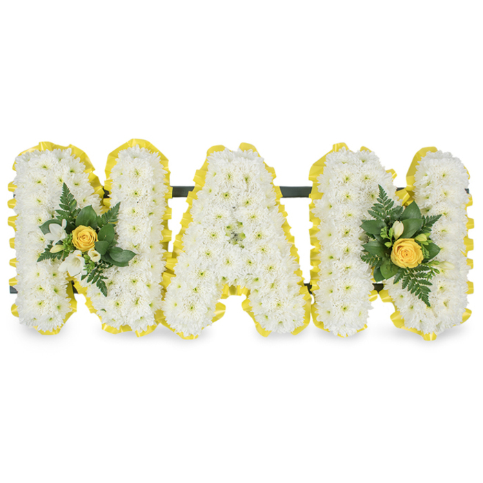 A lovingly composed floral tribute spells MAM in three individual capital letters, each letter formed from a compact carpet of fresh white chrysanthemum spray blooms that create a soft, intricate texture across every face. The perimeter of each letter is neatly finished with a bright, sunny yellow satin ribbon, pleated to give a tactile, uplifting border that visually lifts the white surface and adds a cheerful warmth. The letters are mounted on a slender dark horizontal bar along their upper edges for stability, indicating a freestanding display ready for funeral or memorial placement. Two tasteful embellishment clusters have been positioned for balance: one on the left upright of the first M and the other mirroring it on the right upright of the second M; each cluster is centred on a tightly furled yellow rosebud and framed with sprigs of white freesia, fern fronds and glossy deep-green leaves, the richer foliage bringing depth and a fresh, cool contrast. The overall effect is both dignified and tender - the white chrysanthemums read as purity and the yellow accents as gentle warmth - set against a plain white background so every detail reads clearly. Imagine this tribute arriving for a funeral service in Mill Hill, perhaps placed near a memorial table at St Paul's or beside a family photograph at a church in Mill Hill Village; it carries the quiet craftsmanship of a local florist and the intention to comfort, commemorate and celebrate a much-loved mother figure.