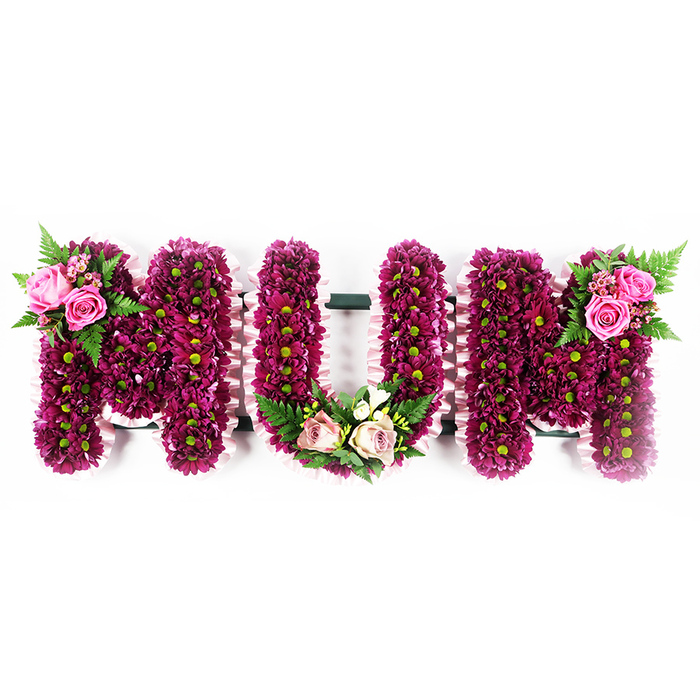 In this image, a meticulously crafted floral arrangement spells MUM in large capital letters, each one rendered as a solid, three-dimensional form and showcased against a bright white background. The face of every letter is saturated with small fuchsia-purple and magenta spray chrysanthemums, positioned tightly side by side so they form an even, cushion-like surface. Their subtle green centres add delicate pinpoints of contrast, lending the tribute a natural, garden-fresh quality despite its formal structure. Running neatly around the sides of the letters is a soft, ruffled ribbon in the palest pink, carefully gathered and smoothed to follow every contour. This ribbon border adds a gentle, almost vintage softness, like the trim on a carefully kept keepsake. On the upper left of the first M, two open blush roses and several rosebuds rest against a backdrop of feathery fern fronds and glossy greenery, giving the impression of a small posy laid lovingly atop the letter. At the base of the central U, a curved cluster of lighter pink roses and creamy white blossoms is nestled among bright green ferns, echoing the shape of the letter and drawing the gaze gently towards the centre. The final M carries a mirrored accent on its upper right, with vibrant pink roses and ferns providing balance and harmony across the design. This personalised MUM tribute, just the sort of arrangement created by Flowers Mill Hill for services in Mill Hill, Hendon, and nearby communities, offers a graceful and heartfelt expression of remembrance for a much-loved mother, with every detail speaking of care, devotion, and lasting respect.