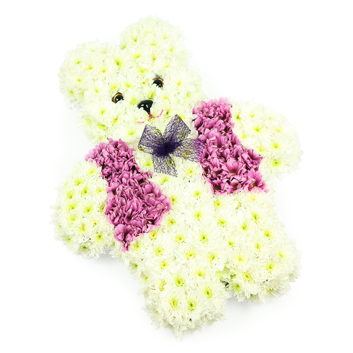 A beautifully detailed teddy bear crafted from flowers sits centered in the frame, photographed against a pure white background so that every nuance of petal and colour is clearly defined. The bear's entire body is formed from closely packed white chrysanthemums, their gently ruffled petals overlapping like layers of soft fleece. The blooms create a rounded, cuddly silhouette, from the slightly domed head and perky ears to the solid torso and short, comforting arms and legs. The white petals are enriched by faint touches of cream and pale lemon at their centers, giving the bear a gentle glow instead of a stark whiteness. Two small, dark, button-like eyes lend a steady, compassionate gaze, while a petite black triangular nose completes its familiar teddy bear look. Just beneath the nose, a suggestion of a smile is shaped by the careful placement of delicate pink-tinted petals, creating an expression that feels calm and reassuring. Draped over the bear's front, a waistcoat made entirely from deep pink and magenta chrysanthemums offers a vivid yet respectful burst of colour, its blooms densely gathered to create defined, vest-like panels. At the neckline, a bow formed from fine violet netting is tied in simple loops, adding a touch of lightness and charm. The even, soft lighting and uncluttered backdrop help focus attention on the careful craftsmanship and freshness of each bloom. This tribute, the kind of piece often prepared by Flowers Mill Hill for services around Daws Lane, Mill Hill Broadway, or local chapels, is particularly meaningful for children's funerals, baby memorials, or commemorative services where innocence, love, and gentle remembrance need a tender symbol.