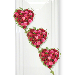 Three luxurious hearts made entirely of roses form the centre of this image, arranged in a gently descending line that feels as serene as an early morning walk through Mill Hill Park. Each heart is densely packed with roses in a harmonious palette of deep red, hot pink, and soft blush, their petals overlapping and interlocking so completely that the surface looks like a rich, floral tapestry. The deep crimson roses bring a sense of depth and solemn devotion, while the brighter pinks add warmth and emotional light, offset by the occasional pale petal that softens and brightens the overall effect. Within the hearts, the roses vary in size and stage of bloom, from tight buds to fully opened flowers, giving an intricate, layered texture that suggests both the intensity and the gentleness of love. Fine strands of ivy outline each heart, the small green leaves hugging the shape and then trailing downwards to link the three hearts together, like a visual echo of family ties or lifelong friendships. The clean white background, similar to a freshly painted wall in a Mill Hill chapel or a peaceful space near Mill Hill East, contrasts crisply with the lush colours of the roses and foliage. Gentle shadows cast behind the hearts create a sense of depth, making them appear almost suspended. The arrangement conveys profound affection and remembrance, making it ideal for a funeral, memorial, or celebration of life. It feels like a bespoke piece carefully crafted for a local family, reflecting the thoughtful artistry and experience of a Mill Hill florist who knows how to express love, loss, and gratitude through flowers.