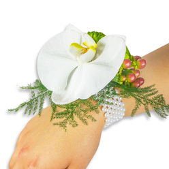 This refined wrist corsage is presented on a light-toned wrist against a clean white field, designed to showcase craftsmanship and the natural beauty of its elements. Dominating the composition is a pristine white Phalaenopsis orchid whose broad, velvety petals unfurl with calm confidence; the orchid's lip holds a bright yellow center flushed with deeper orange that draws the eye like a small, sunlit heart. Nestled beneath and around the bloom, soft sprays of asparagus fern create a green, feathery cushion that breathes movement into the arrangement and provides a tactile contrast to the orchid's satin surface. Tucked to the upper right, a cluster of Hypericum berries moves through a spectrum of tones - from pale green to blushing rose and rich crimson - offering a seasonal pop and a rounded, glossy texture. Small ruffled lime-green foliage amplifies the textural layering and lifts the palette. The whole design is mounted on a classic, multi-strand pearl bracelet that curves comfortably around the wrist, the pearls' pearly sheen complementing the orchid's whiteness and suggesting quiet formality. The mood is gentle, ceremonial and suited to weddings, proms or a special anniversary. As crafted by Flowers Mill Hill, this corsage balances modern simplicity with traditional accents and would sit beautifully at events across Mill Hill Broadway, The Ridgeway, or a reception near Bittacy Hill - a small, wearable arrangement that reads as both intimate and impeccably put together.