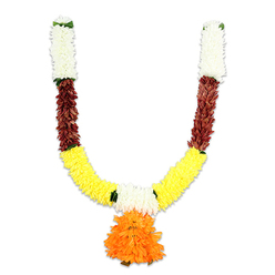 A U-shaped decorative mala, photographed on a stark white background so every colour and texture reads clearly, reveals traditional form with contemporary durability. At the very top of each curved arm a compact column of creamy white florets-soft, cushiony forms echoing small chrysanthemums-creates a light, airy crown; tiny flashes of green at the seams suggest leaflets or ribbon loops used to secure the strands. Directly below, each arm yields to a compact, russet-red or reddish-brown section whose flattened, layered petals bring depth and a natural, earthen tone that grounds the design. The garland then opens into a broad sweep of bright, golden-yellow clusters, densely threaded and fluffy in feel, strongly evocative of marigold strings used in auspicious Indian rituals. Suspended where the two arms meet is a voluminous orange pendant: many ruffled layers gather into a rounded, sunburst-like tassel that commands visual focus and adds lively movement. The construction reads clearly as high-quality artificial materials-silk-like fibres and resilient cores-intended to mimic fresh flowers while offering long-lasting use for doorways, mandaps and altar displays. Under soft studio lighting the petals glow with saturated warmth, and the subtle contrast between creamy white, deep russet and vivid yellow-orange feels both celebratory and reverent. As a Mill Hill florist would note, this toran blends festival colour with practical longevity and is the kind of adornment you might see brightening porches and community halls around Mill Hill Village and The Ridgeway during Diwali and wedding season. The overall effect is traditional, auspicious and thoughtfully made.