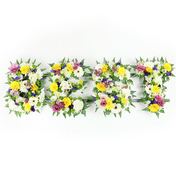 Centered horizontally on a stark white background, four bold letters form the word BEST in a lush, handcrafted floral display, each letter built from a tight mass of fresh blooms and greenery. The overall tone is bright and reassuring: pristine white chrysanthemum-like flowers and ivory spray carnations provide a soft, pure foundation, while cheerful yellow roses and gerbera daisies bring warmth and optimism. Accents of gentle lavender and deeper purple lisianthus or smaller chrysanthemums give subtle spiritual depth, and splashes of magenta-pink spray roses or carnations add poignant vibrancy. Interspersed clusters of light green and white filler flowers create tactile texture between larger heads, and generous fern fronds form a dark green border that both defines the letter shapes and softens their edges. Where the arrangement is less dense, a dark green or metallic support frame shows through-notably along the horizontal bar of the E and the top cross of the T-revealing the skilled engineering beneath the floristry. Photographed head-on with bright, even light, the display emphasizes freshness, colour contrast, and the gentle shadowing that rounds each bloom. This dignified piece is often chosen as a funeral or memorial tribute to describe a dearly loved person as the best; its readable typography makes it suitable for chapels and church displays. As a local Mill Hill florist would advise, the palette reads well on camera and from a distance, and Flowers Mill Hill can prepare similar bespoke tributes for services across Mill Hill and the NW7 area with the same attention to scent, texture and structure.