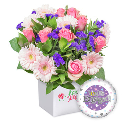 From a Mill Hill vantage, this congratulatory bouquet feels crafted for the everyday celebrations of North London life. The white square box reads as a modern frame for a garden of pinks: soft pink roses in varying maturities-buds tight as promises, open blooms warm with romance-paired with gerberas in pale pink with crisp white edges and soft yellow centers that glow like morning sun on a station platform. The mix is punctuated by clusters of deep purple statice or limonium, adding a note of cinematic depth and contrast against the lush green foliage that spills around the stems, suggesting a quiet garden in a city courtyard.

The presentation box itself is sleek and clean, inviting a close look at the blooms, and the subtle branding on its front (a red rose icon with green script) nods to the artistry of a local florist without shouting. In the lower right, a round foil balloon floats, coordinating with the bouquet in celebration. The balloon's central purple circle hosts the silver inscription "You're Engaged!", with the golden 'O' stylised as a sparkling ring, a playful detail that catches the eye on a busy kitchen table or windowsill. The white outer ring is dotted with tiny pastel hearts and delicate silver stars, echoing the romantic mood.

This arrangement is ideal for couples in Mill Hill looking to mark a new chapter-whether it arrives as a surprise at home or an office delivery along The Broadway. It conveys warmth, happiness, and hopeful anticipation, and can be ordered for same-day delivery across Mill Hill, Mill Hill East, and nearby neighbourhoods, helping celebrate a moment that brings people together in the local community.