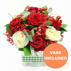 A beautifully composed bouquet of red and white roses stands out against a bright white background, captured with the kind of care you'd expect from experienced florists serving Mill Hill. The deep red roses, velvety and luxuriant, form the passionate core of the design, each bloom unfurling in layered spirals that draw the gaze inward. Intertwined with them, creamy white roses bring gentle luminosity, their petals slightly curled at the edges, offering soft contrast and a sense of calm refinement. Between these classic blooms, delicate clusters of tiny red filler flowers, reminiscent of dyed gypsophila, weave a fine, airy texture that lightens the arrangement, like a subtle red mist drifting through the petals. Rounded, glossy red hypericum berries punctuate the bouquet at intervals, their smooth, bead-like forms reflecting light and adding visual rhythm. Around the flowers, eucalyptus sprigs and varied green foliage extend outward, creating a halo of greenery that adds structure, movement, and a hint of fresh, herbal fragrance, akin to a stroll through the leafier streets near Mill Hill Park or Daws Lane. The stems are gathered in a clear, rectangular glass vase, its straight edges and see-through sides giving a modern, uncluttered feel while allowing the stems and water to become part of the composition. Wrapped snugly around the vase is a green and white gingham ribbon, introducing a rustic, homely note that suggests cosy kitchens and relaxed family celebrations in Mill Hill homes. In the bottom right corner, an orange circular graphic clearly displays the words "VASE INCLUDED" in white capitals, making it evident that this arrangement arrives complete and ready to place, ideal for birthdays, anniversaries, or elegant same-day flower deliveries across Mill Hill.