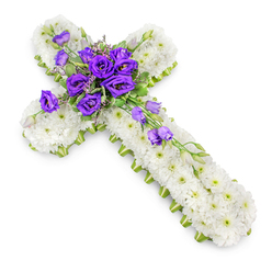 This image shows an elegant Christian cross made entirely from fresh flowers, photographed from above against a bright, uncluttered white background. The cross is tightly packed with white spray chrysanthemums, their petals forming a soft, almost quilted layer that stretches seamlessly from the top of the vertical arm to the base. In each bloom, a pale green centre peeps through, dotting the surface with subtle, natural highlights that stop the white from feeling stark. A slim ribbon or edging of lime-green traces the outline of the cross, running along its sides in a continuous band and neatly emphasising the clean, symmetrical silhouette. At the heart of the cross, at the intersection of the arms, sits a striking arrangement of deep purple lisianthus flowers. Their layered petals fold inwards in soft spirals, rich in colour and texture, creating a focal point that feels both solemn and beautiful. Scattered through this central cluster are touches of fresh foliage, some fine filler flowers, and small purple buds at different stages of opening, adding depth and a sense of gentle movement. From the centre, a short cascade of lisianthus blooms and buds flows diagonally down the right-hand side, as if the colour is quietly spreading along the arm. The lighting is even and bright, with a soft shadow beneath the cross that gives the design a sense of presence, as if it rests carefully on a white table in a Mill Hill studio. This floral cross would be a thoughtful choice for a funeral service near Mill Hill East or a memorial gathering around Bittacy Hill, reflecting comfort, faith, and loving remembrance.