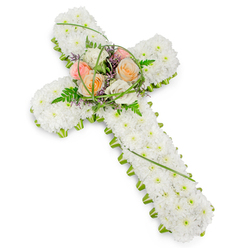 This photograph captures a traditional Christian cross interpreted through flowers, exquisitely detailed and set against a spotless white background that emphasises its structure and symbolism. The main body of the cross is entirely covered with pristine white chrysanthemums, closely packed together so that their small, rounded petals form a soft, even field of white, evoking purity, prayer, and gentle remembrance. Around the perimeter, a sharp but natural border of vivid green foliage defines the outline, creating a clear contrast much like the crisp edges of lawns and tree lines you might see along Bittacy Hill or around Mill Hill Broadway. At the intersection of the cross's arms, a central spray rises slightly above the base layer of flowers, offering a tender focal point. Here, roses in muted peach, pale coral, blush pink, and creamy white unfold in generous, open blooms, their petals appearing almost velvety to the touch. Around and between these roses, feathery ferns and small leaves weave a soft green cradle, while fine, arching blades of bear grass add graceful curves and a sense of movement. Tiny touches of purple filler flowers glimmer discreetly, adding depth to the otherwise soft pastel and white palette. The whole arrangement feels peaceful and composed, an ideal funeral tribute for a chapel or crematorium service serving the Mill Hill community. The cross symbolises faith and eternal rest, while the warm-toned roses speak of love, gratitude, and farewell, making the design a comforting presence for mourners gathered to say their final goodbyes.