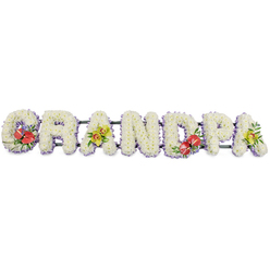 The image presents a beautifully composed funeral flower tribute spelling out the word GRANDPA in large, block capital letters, arranged in a straight line against a plain white background. Each letter is filled to the brim with tightly packed, small white chrysanthemums, the rounded petals overlapping in layers to form a soft, cushion-like surface. This expanse of white gives the tribute a sense of purity, calm, and quiet respect, ideal for a final farewell. Along the lower edge of every letter, a fine band of pale lavender ribbon creates a subtle outline, introducing a cool lilac tone that gently defines the shapes without overpowering the simplicity of the white blooms. Behind the flowers, dark green framework supports and links the letters, ready for the tribute to be placed on display at a funeral in Mill Hill, perhaps near Mill Hill Park or a local place of worship where families gather to remember a grandfather. Carefully chosen accent flowers add emotion and colour. On the G and the central D, deep red anthuriums cluster among rich green foliage and tiny purple filler flowers, their waxy, heart-shaped petals and prominent spadices creating focal points that speak of deep love and remembrance. The first and last A are softened by sprays of yellow-green orchids, their graceful, exotic blooms introducing a touch of sophistication and hope. Together, these elements form a bespoke sympathy tribute, the sort of lovingly made arrangement a Mill Hill family might order when they wish to say goodbye in a way that feels personal, respectful, and full of gratitude for a grandfather's life.