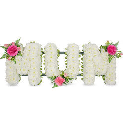 This image presents a tender memorial arrangement spelling out "MUM" in large, confident block letters, photographed straight on so the full shape and texture of the tribute are clearly visible. The letters rest on a dark green framework that subtly peeks through at the base, ensuring the tribute can be displayed securely beside a coffin, on a stand, or near a photograph during services in Mill Hill and neighbouring areas like Edgware or Totteridge. Every surface of the lettering is densely blanketed with small white spray chrysanthemums, their compact heads and layered petals forming a plush, almost quilted appearance. The whiteness feels calm and cleansing, with slight shadows between the blooms hinting at depth and dimension. On this pure canvas, three matching accents of vivid colour and fresh foliage bring warmth and individuality. At the upper left of the first "M," a bright fuchsia garden rose unfurls, framed by softer blush-pink spray roses and partially opened buds that suggest ongoing life and memory. Fine fern fronds curve around the blooms, adding a touch of natural movement. The central "U" carries its own cluster at the lower middle, nestling into the letter's curve, while the upper right of the second "M" holds the final group of pink roses and fern. Together they form a gentle diagonal rhythm across the arrangement. The overall effect is one of quiet elegance, the kind of bespoke floral lettering often chosen by Mill Hill families to honour a mother's love at a funeral, memorial, or graveside visit.