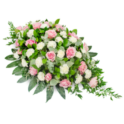 Displayed against a bright white backdrop, this large sympathy spray showcases a graceful, elongated teardrop form, the kind often chosen as a casket spray or main tribute at a funeral in Mill Hill. The eye is immediately drawn to the abundance of pastel pink roses, each bloom carefully placed so that their spiralling petals create a gentle rhythm along the length of the design. Some roses are just beginning to open, promising softness, while others are fully unfurled, their layered petals catching the light and adding dimension. Nestled between the roses are clusters of white carnations and spray carnations, their ruffled, cloud-like textures giving the arrangement a plush, embracing quality. The palette of blush pink and pure white remains soothing and understated, echoing the quiet, reflective atmosphere of a chapel service or a wake in a family home near Mill Hill East or along the quiet residential streets off Bittacy Hill. Beneath and around the flowers, rich greenery provides both structure and contrast: smooth, glossy dark green leaves frame the spray, while round, silvery eucalyptus leaves soften edges and fill spaces with a subtle, cool-toned haze. From the slender, pointed end of the design, delicate strands of trailing ruscus flow outward, adding light movement and completing the teardrop shape. The arrangement is rounded and full at the top, then gently narrows to a defined point, like a symbolic tear of farewell. The feeling it conveys is one of quiet luxury, compassion, and remembrance, a thoughtfully composed floral tribute that offers comfort and a touch of natural beauty during difficult goodbyes in the Mill Hill community.