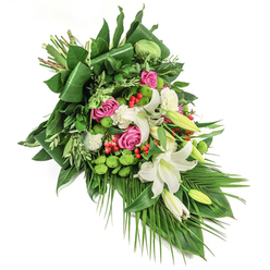 Evoking the serene landscapes and community spirit of Mill Hill, this artfully designed diagonal funeral spray is a celebration of life and memory. Resting on a stark white backdrop, the eye is led by the graceful sweep of the arrangement from top left to bottom right-an echo of the gentle slopes beyond Mill Hill Broadway. White lilies, with their open trumpet petals and golden stamens, exude a sense of peace and tribute, while closed buds nestle beside them, representing hope and continuous remembrance. Clusters of deep pink and fuchsia roses bloom between, their velvety petals offering warmth and sympathy. Textural accents appear in crisp white spray carnations and modern, vivid green santini chrysanthemums whose round, mossy heads provide a lively pop of colour. Crimson hypericum berries are scattered throughout, drawing the gaze with their cheerful energy and natural sheen. Abundant rich green foliage forms the foundation: from streamlined broad leaves-some artfully folded-to unfurling palm-like fronds and feathery, lighter greens that lend both structure and softness. Each flower and stem is selected by local Mill Hill florists, their expertise evident in the harmonious combinations and elegant flow. Bathed in gentle daylight, the bouquet radiates with intention, making it a comforting choice for farewells, standing as a thoughtful expression of respect, compassion, and enduring love throughout the Mill Hill area.