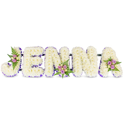 This bespoke memorial arrangement reads the name "JENNA" in sculpted, uppercase letters formed from hundreds of creamy white chrysanthemums or similar petite blooms, each petal layered to create a pillowy, reverent texture against a plain white surface. A slender border of rich purple ribbon or tiny lavender blooms traces the inner contours of each letter, providing crisp contrast and a refined silhouette that allows the letters to sit with quiet dignity. Three small, hand-tied clusters soften the geometry: blush-pink and pale lavender spray roses, with a few creamy yellow roses and dark green fern fronds, are artfully nestled into the 'J', the middle of the first 'N', and the top right of the final 'A', introducing gentle warmth and subtle colour notes. The letters are united by slim, dark horizontal connectors that indicate a sturdy floral frame built for display at a funeral, memorial service, or celebration of life. The scent is understated-green chrysanthemum earthiness with a whisper of rose-while the texture invites a compassionate, reverent touch. Having created many such name tributes for families across Mill Hill Village and around The Ridgeway, Flowers Mill Hill understands how a personalised floral name can act as a comforting, visual tribute during grief. The arrangement is designed to be viewed from the front, where the white field and purple edging read cleanly in chapel lighting, yet it rewards a closer look with the handcrafted clusters that speak of tenderness, remembrance and enduring affection.