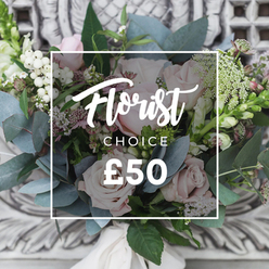 Soft blush roses lead the eye in this loose, garden-style bouquet, their layered petals forming gentle, romantic domes against a backdrop of silvery-blue eucalyptus. Interspersed throughout are bright white, rounded berries that catch the light and add fresh contrast, while sprays of tiny white waxflower or astrantia breathe an ethereal, meadow-like quality into the arrangement. Deeper pink and burgundy buds peek through in places, lending depth and a whisper of warmth beneath the pale palette. Tall, vertical flower spikes-reminiscent of snapdragons-emerge at the sides, giving the bouquet a natural, slightly architectural rhythm that feels both relaxed and intentional. Texturally the piece is rewarding: the velvety rose heads, the crisp prickle of greens, and the smooth, cool eucalyptus leaves create a tactile richness you can almost feel. A soft cream ribbon secures the hand-tied stems, suggesting a bespoke finish ready for delivery or display on a carved mantel. The image is captured in soft ambient light that enhances the bouquet's quiet elegance; in Mill Hill this is the sort of arrangement local customers choose for a thoughtful birthday gift, a welcome for a new home, or to lift someone's day. The overlayed white frame and typography identify it as a florist's choice at around £50, signalling a trusted selection of seasonal blooms chosen for harmony and freshness rather than rigid formality.