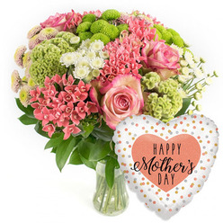 This photograph presents a beautifully composed Mother's Day bouquet and balloon, styled as a product image for a Mill Hill flower delivery service. The arrangement rests in a simple clear glass vase, positioned slightly left of centre against an uninterrupted white background that highlights every colour and contour. The bouquet forms a neat, domed shape, brimming with varied textures. At its heart are several full pink roses, their layered petals deepening to a richer pink around the edges, creating a soft halo effect. Encircling them, clusters of coral-pink blossoms, similar to kalanchoe, pack in tight little florets that bring a sense of movement and energy. Lime-green button chrysanthemums offer vivid accents throughout the design, their rounded, tufted heads adding contemporary flair and a refreshing contrast to the warm pinks. White daisy-like spray chrysanthemums are tucked between the bolder blooms, lending small flashes of brightness and a gentle, airy balance. Rich dark green foliage lines the base and threads through the bouquet, giving it depth and anchoring the lighter tones. To the lower right, a heart-shaped foil balloon rises into the frame. Its surface appears smooth and metallic, with a white or very pale silver background dotted with irregular specks of gold and soft peach-silver, reminiscent of celebratory confetti scattered at a family lunch in Mill Hill. At the centre of the balloon sits a peach-toned heart bearing the phrase "HAPPY Mother's DAY" in stylish black script and capitals. The scene conveys the warmth of thanking Mum with flowers arranged by a local Mill Hill florist, perfect for homes near Mill Hill East station, the Broadway, or the quiet residential roads leading toward Hendon.