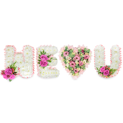 Viewed close-up, the message H E (heart) U is rendered in meticulous floral craft: three letters and a heart, each element shaped and finished with an exacting florist's eye familiar to our neighbourhood around Mill Hill Broadway and The Ridgeway. The H, E and U are built from densely packed white chrysanthemums that create a pillowy, matte surface; their edges are traced with a delicate blush-pink satin ribbon that whispers of care and keeps each shape distinct. Vibrant fuchsia roses act as focal punctuation - a compact accent of two roses and tiny red berries at the base of the H's left stroke, a central trio on the E's middle arm, and a matching pair tucked into the inner curve of the U - all cushioned by dark green, fern-like foliage for structure. Between the letters sits a full heart, softer in tone: a layered blend of pale pink carnations, gentle blush lisianthus or small roses, and pale green eucalyptus leaves that add texture, cooling colour and a subtle aromatic lift. The ribbon outline unifies the piece and the contrasting greens give depth beneath the pinks and whites. This composition - appropriate as a sympathy tribute, celebration of life piece, or an intimate declaration - reads as both tender and dignified. Created by a Mill Hill florist, the arrangement reflects local sensibilities and care, and would suit delivery to a chapel or family home in Mill Hill Village or for placement near Mill Hill Park, where its scent and quiet palette would feel perfectly at home. Flowers Mill Hill prepared this with the gentle restraint such moments deserve.