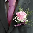 There is a sense of gentle poetry in this Mill Hill boutonniere, where every detail works in harmony to convey warmth, elegance, and joyful anticipation. At the core sits a blush-pink rose, its petals gently unfurling as though echoing the quiet beauty of sunrise over Mill Hill's rolling commons. The bloom's fresh fragrance, barely perceptible, hints at new beginnings-ideal for a wedding morning or an evening of celebration on Bittacy Hill. Surrounding the rose, sprigs of baby's breath add cloud-like softness and a touch of nostalgia, inviting memories of picking wildflowers along local footpaths. Wispy green foliage forms a delicate arc, infusing the arrangement with natural movement and grounding it in the area's leafy heritage. The piece is anchored by a satin lavender ribbon, glossy and soft to the touch, which secures the countenance elegantly atop a charcoal suit lapel. The composition is finished with a bright fuchsia tie and a subtle grey shirt, together highlighting the careful interplay of fresh pastels and contemporary styling so emblematic of Mill Hill. Designed with heart, this boutonniere brings together artistry, locality, and a sense of celebration in every petal and ribboned touch.