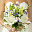 A masterful bridal composition that reads as refined and naturally luminous, this bouquet centers on large, star-shaped white lilies whose velvety petals unfold with graceful ease. The lilies form a calm, radiant heart to the design while purple-tinged lisianthus, edged and ruffled, slip between the larger blooms to provide cool contrast and gentle depth. Tiny veronica spikes and delicate clusters of baby's breath nod through the arrangement like quiet punctuation marks, adding vertical accents and a soft, intricate texture that draws the eye inward. Wisps of fine green grass and slender foliage create movement, a light halo that seems to flutter when the bouquet is carried down the aisle. In this composition the tactile differences are important - the lilies' satin surfaces, the lisianthus' frilled edges, the feathery greens - all selected and layered so each stem contributes to a balanced silhouette. The scent is a restrained, pleasing blend: lily sweetness with green, dewy undertones that evoke early-morning gardens. In Mill Hill, where weddings range from village hall receptions to elegant rooms near Mill Hill Broadway, this bouquet offers a timeless presence with a contemporary lift. As a Mill Hill florist I think of how it photographs in soft daylight or against the warm brick of local churches. Hand-tied with care and attention to proportion, it is a design intended to be carried, cherished, and remembered - and is available for delivery across Mill Hill and surrounding NW London when requested through Flowers Mill Hill.