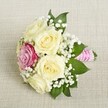 A compact, elegantly styled bouquet rests atop a creamy linen fabric, mirroring the refined simplicity beloved by Mill Hill residents. Centrally arranged are creamy white or pale yellow roses, their gently unfurling petals exuding softness and warmth. Slightly off to one side, a vivid magenta rose provides a burst of color, evoking the spirited look of local park blooms. Lacy clusters of white baby's breath weave lightness through the design, while deep green foliage outlines the bouquet with subtle freshness. The stems are expertly bound with textured pink satin ribbon, spiraled with pearly beads that catch the soft, ambient light-an effect both sophisticated and joyful. This arrangement, whether intended for an intimate garden wedding, a stylish bridal party, or a heartfelt Mill Hill celebration, radiates classic charm and bespoke craftsmanship unique to the local floral scene.