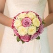 Effortlessly elegant and imbued with a sense of fresh beginnings, this bridal bouquet shines in the natural light of a Mill Hill afternoon, held lovingly at the bride's waist and forming the focal point of this close-up image. The bouquet is a harmonious blend of creamy ivory and pale lemon-yellow roses, each tightly gathered yet brimming with delicate freshness, accompanied by vibrant fuchsia pink and mauve-toned roses that add a lively, playful twist. Intertwined throughout are soft, cloud-like sprigs of baby's breath, providing a gentle, floating effect that enhances the bouquet's romantic air. Rich green leaves peek discreetly from beneath, grounding the arrangement in the verdant local character so often found in Mill Hill's suburban gardens and parks. The bride's relaxed arms frame the flowers, her dress an ode to tradition with its intricate lace details on the bodice and a smooth, flowing skirt that cascades softly with every movement. Illuminated by steady, flattering light, the bouquet and dress each reveal exceptional detail-rosy textures, lace filigree, and the careful artistry of a local florist. The background is softly obscured, suffused with a calming brightness that centers the viewer on the tenderness of the moment. For brides seeking a floral arrangement as special as Mill Hill itself, this bouquet is a symbol of joy and unity, evocative of a celebration among family and friends in the heart of North London.