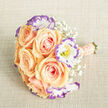 This photograph captures a bridal-style hand-tied bouquet laid on coarse, light beige fabric that resembles natural linen, the texture anchoring the composition much like the familiar stone surfaces around Mill Hill Broadway. The bouquet centres on six to nine soft apricot-peach roses, their petals folded in luscious spirals that glow from the inside out and suggest the warmth of first light. Interwoven among them are white lisianthus with delicate ruffled edges tipped in violet-purple, each bloom revealing a tiny yellow stamen that adds a crisp dot of contrast. Cloud-like sprays of baby's breath weave through the arrangement, creating gentle negative space and an airy, ethereal backdrop that allows the roses and lisianthus to sing. The handle is wrapped in a coordinating blush-peach ribbon and embellished with multiple rows of small cream pearls, a tactile, elegant finish that would sit comfortably in a bride's hand as she walks from Deansbrook Road toward The Ridgeway. The trimmed green stems are visible at the base, clean and fresh-cut, while soft, even lighting sculpts petal textures and subtle tonal shifts. As a Mill Hill florist I picture this bouquet delivered to an intimate ceremony at a local church or set upon a mantle in a village home; Flowers Mill Hill would prepare it with attention to balance, scent, and seasonal freshness. Overall, the arrangement reads as tender, refined, and quietly celebratory - the kind of piece that marks a milestone with gentle beauty and local care.