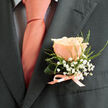 This boutonniere, prepared by Flowers Mill Hill for ceremonies across Mill Hill and the surrounding streets, balances celebration and restraint with florist's care. A single, flawless peach rose rests on the lapel, its blush-coral petals layered like morning light and catching a soft sheen that complements a matching tie. Encircling the rose, clusters of white gypsophila provide a frothy, ethereal contrast-tiny, cloud-like blossoms that lend innocence and a light, confetti-like impression. Fresh greens thread through the arrangement, their textures ranging from crisp leaf edge to slender, airy fronds, giving structure and a lively, natural rhythm.

Tied with a narrow satin ribbon in a soft peach tone, the stems are finished into a tidy bow that reflects the careful handiwork of a neighbourhood florist serving Mill Hill Broadway, The Ridgeway and nearby Bittacy Hill. The charcoal of the suit deepens every hue, making the coral-pink glow of the rose more luminous and the white gypsophila more luminous by contrast. There is an implied scent - a subtle, sweet perfume that suggests optimism and devotion - and tactile details: the rose's velvet petal, the baby's breath's whispery texture, and the smoothness of satin against wool. Designed for a groom or honoured guest, this boutonniere carries quiet assurance: a miniature composition that reads as tradition, tenderness and celebration-perfect for a wedding, anniversary or any moment in Mill Hill where small gestures mean everything.