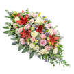 A beautifully composed, double-ended casket spray is shown against a clear white background, every bloom and leaf arranged with the precision and care you might expect from Flowers Mill Hill for a final farewell. The arrangement is elongated and symmetrical, widest through the centre and gently narrowing towards both ends, designed to sit gracefully along a coffin during a funeral service. Dominating the piece are vibrant deep red Oriental lilies, their large star-shaped petals opening wide, with darker markings adding drama and depth. These bold flowers are surrounded by an abundance of roses in cream, soft blush pink, and pale pastel tones, each rose at a different stage of opening, from shy buds to fully unfurled blossoms, conveying tenderness, respect, and long-lasting love. Pale pink spray carnations, intricately ruffled, weave through the spray, adding softness and volume, while white chrysanthemum-style blooms and tiny white daisies bring brightness and a sense of purity. Cool-toned accents of spiky blue-purple thistles and small bunches of lavender or statice thread between the warmer colours, echoing the gentle hues of an evening sky over Mill Hill's parkland. The flowers sit on a generous bed of deep green foliage-broad, glossy leaves for structure, feathery fern-like sprigs for lightness, and trailing greenery that extends delicately beyond the main outline-giving the design an organic, flowing feel. Overall, the spray conveys quiet elegance and heartfelt sympathy, a comforting floral tribute intended to honour and remember a loved one at a funeral, cremation, or memorial service in and around Mill Hill.