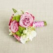 A small, hand-tied bouquet lies horizontally on a softly textured, light tan fabric that looks like natural linen, the neutral backdrop allowing every flower to stand out clearly. At the heart of the arrangement, three open pink roses unfurl in lush spirals, their petals moving from gentle blush at the centre to deeper, almost magenta pink along the outer edges, creating a subtle ombre effect that feels both modern and romantic. Nestled between the roses are perfectly round lime-green button chrysanthemums, their tiny packed florets forming playful pom-pom shapes that add a crisp, contemporary contrast to the softness of the roses. Around them, clusters of creamy white and ivory filler blooms, reminiscent of lisianthus, freesia, or waxflower, bring an airy lightness, with a few tiny star-shaped blossoms and yellow centres adding intricate detail. The stems are gathered into a short, neat handle on the right-hand side, tightly wrapped in vivid fuchsia satin ribbon that gleams softly in the even, natural light. A fine strand of white faux pearls winds diagonally across the ribbon, like a delicate bracelet, lending a graceful, bridal touch. The green stems extend just beyond the ribbon, freshly cut and perfectly aligned. The overall mood is of poised elegance and fresh romance, the sort of posy you might see carried along Mill Hill Broadway on the way to a wedding at a local church or a celebration in one of Mill Hill's leafy venues, ideal as a bridesmaid bouquet, petite bridal posy, or a refined centrepiece for an intimate gathering.