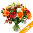 A vibrant, hand-tied autumn bouquet stands against a crisp white background, every element arranged to celebrate the season. At its heart sit several open orange lilies, trumpet-shaped and wide-petaled, their prominent stamens adding a dark, sculptural contrast to the warm floral palette. Around them, ruby-red and bright-orange Gerbera daisies fan their concentric petals like small suns, while clusters of smaller orange spray blooms tuck into the spaces, giving the composition cheerful density. Soft, ruffled white Lisianthus provides cool, creamy highlights that catch the light and soften the overall warmth, and star-like Astrantia with purple-pink centers lends delicate, architectural texture that invites a closer look. The flowers rest on a base of lush deep-green foliage-likely ruscus or salal-whose glossy leaves create a verdant backdrop. Scattered through the design are large, deeply lobed oak leaves in rich reddish-brown and burnt-orange tones; their jagged silhouettes introduce autumnal structure and a woodland feel. The stems are neatly gathered and bound with dark twine or raffia, showing traditional hand-tied craftsmanship and a natural, rustic finish. The lighting is even and clean, making petals appear luminous and the foliage richly saturated, as if placed in soft morning light from Mill Hill Park. In the lower right corner of the image a bright orange diagonal banner reads FREE CHOCOLATE in bold white letters, a clear visual overlay indicating an included promotional item. This bouquet feels perfectly suited for a Mill Hill birthday, a warm thank-you, or a seasonal gift, offering both the tactile freshness of just-cut stems and the comforting colours of an October afternoon.