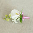 Set against a subtly textured, natural linen background in a soft oatmeal shade, this boutonniere appears almost like a small painting in three dimensions. At the centre, a flawless white Phalaenopsis orchid unfolds, its wide, velvety petals forming an elegant oval that draws the eye inward. In the orchid's throat, a whisper of yellow-orange and the lightest touch of pink bring warmth to the cool white, evoking the gentle glow of early morning light over Mill Hill's quiet streets. Around this focal bloom, airy clusters of white Gypsophila, known as baby's breath, gather like tiny clouds, their countless little flowers creating a romantic haze that softens every edge. Slim, bright green leaves weave through the composition, giving structure and a crisp contrast, as if echoing the fresh greenery you might see on a walk through Mill Hill Park after a spring shower. To the left, a single side stem bears three rounded, pale green orchid buds, still tightly closed, suggesting the promise of blossoms yet to open and symbolising new chapters in life. At the base, the stems are wrapped with a lustrous pink satin ribbon, tied neatly into a compact bow whose short tails sit smoothly against the fabric, adding a playful yet refined touch of colour. The overall mood is one of quiet sophistication-perfect for a groom heading to a Mill Hill synagogue, a prom corsage alternative for a local student, or any formal occasion where detail matters. Looking at this boutonniere, you can almost feel the care of a skilled local florist, each element chosen and placed with intention so the wearer carries a piece of living elegance throughout the day.
