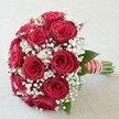 Vivid and elegantly arranged, this bridal bouquet stands out as a modern classic crafted by a dedicated Mill Hill florist. Plump, velvety red roses bloom in abundance, their deep, passionate hue taking centre stage in a dome-like formation that feels both lush and sophisticated. Scattered between the roses, wispy clouds of white baby's breath lighten the overall composition, imparting a soft, romantic air-much like the fresh breeze along Bittacy Hill or beneath the trees of Mill Hill Park. Occasional flashes of dark green foliage peek through, grounding the bouquet and evoking the natural beauty found throughout the area. The bouquet's handle is wrapped in a vibrant red satin ribbon, elegantly striped with white and studded by a twist of lustrous pearls, reminiscent of the subtle, luxe details favoured for celebrations at local venues. At the base, neatly exposed stems affirm the bouquet's freshness and hand-crafted quality. Bathed in clear, natural light, every petal and pearl gleams with vibrancy and hope. This arrangement embodies celebration and romance, making it an ideal choice for wedding days, anniversaries, or declarations of love cherished by the Mill Hill community, and beautifully suited for meaningful moments shared close to home.