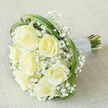 Seven prominent, creamy-white roses form the heart of this classic bridal bouquet, their petals unfurling in soft, layered swirls that read as both luxurious and reassuringly natural. The roses sit amid abundant clusters of tiny white gypsophila, whose minute stars create a soft, cloud-like texture that breathes lightness into the arrangement and offsets the roses' fullness. Woven through the perimeter are graceful ribbons of bright green bear grass, looping in smooth arcs to define the bouquet's silhouette and to add a contemporary, meadow-inspired twist to an otherwise timeless composition. The stems are tightly bound into a firm handle and cocooned in a silvery-white satin ribbon, carefully finished with neat rows of tiny pearl beads that glimmer with subtle iridescence under gentle lighting. Set diagonally on a neutral, warm beige fabric, the bouquet's colours and textures are amplified: the ivory petals glow against the linen and the glossy leaves catch soft reflections. As a florist who knows Mill Hill - from quiet walks along The Ridgeway to arranging for couples at local halls near Mill Hill Park - I picture this bouquet carried with calm confidence, its barely-there rose perfume drifting like a memory. It is equally at home in a small village ceremony, as a tender sympathy tribute, or as an anniversary keepsake; each tactile detail and elegant flourish speaks of careful craftsmanship and an intention to comfort, celebrate, and adorn.