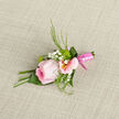 This elegant boutonniere centres on a cool pink rose, its petals unfolding in a soft spiral that feels both refined and inviting, like a whispered promise before a ceremony along Mill Hill Broadway. The rose displays a delicate gradient of colour, with its core holding a richer pink that gradually fades to pale, almost luminescent edges. Around it, pale pink alstroemeria blooms open their slim petals, each marked by gentle streaks of rose and a warm golden hint in the throat, adding subtle complexity and depth. Tiny white gypsophila blossoms dot the spaces in between, their airy clusters creating a cloud-like softness that balances the more substantial blooms. Slender tendrils of greenery arc delicately around the flowers, fresh and vivid, reminiscent of the tidy hedges and leafy paths of Mill Hill Park. The stems are gathered and wrapped in a smooth pink satin ribbon, wound with careful, even pressure so it lies flat and glossy, giving a polished finish that suits a wedding, prom, or milestone celebration at a local North London venue. The boutonniere rests on a textured fabric surface, whose gentle weave frames the piece and hints at smart formalwear. Soft, diffused light enhances every contour, from the velvet of the rose to the crisp line of each leaf, without overwhelming the design. You can almost imagine the light, sweet fragrance and the slight coolness of the petals under your fingertips. Perfect for same-day delivery across Mill Hill and nearby neighbourhoods, this design offers a quietly romantic accent that completes a look without ever shouting for attention.