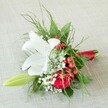 A splendid, hand-tied arrangement rests on a textured, cream-coloured fabric, radiating quiet luxury in the heart of Mill Hill. The centre highlights a wide-open white lily, petals edged with occasionally freckled russet hues, while prominent yellow stamens glow softly beneath the bright natural light. Alongside, a deep red rose swirls in a classic spiral, each velvet petal echoing passionate sentiments cherished at Mill Hill's family celebrations. Sprigs of snowy baby's breath interlace with shining red berries, their playful abundance enhancing the bouquet's festive and inviting mood. A slender, soft green lily bud curves along the edge, signifying hope and fresh beginnings for the coming season. Bound at the base, fine fern-like leaves mingle with dark, glossy foliage, providing a lush, textured frame. Finished with a striking red satin ribbon that echoes the local spirit and the red accents of the florals, this bouquet speaks of sophisticated joy-a popular choice for weddings, proms, or a memorable gift for a loved one in Mill Hill. Its freshness and detail exemplify the care put into every creation by the area's trusted florists.