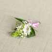 This delicate floral boutonniere is photographed against an oatmeal-coloured woven fabric, the neutral background echoing the quiet charm of residential streets in Mill Hill. The composition is centred around a single, open white alstroemeria flower, whose broad petals curve gracefully outward, their surface smooth and almost satiny. Inside, fine maroon-brown streaks trace the throat of the bloom, adding depth and a touch of character to the otherwise pristine white. Nestled closely beside it are smaller white buds and partially opened flowers, recalling lily-of-the-valley with their petite, bell-like forms and gentle curves. Tiny sprays of white gypsophila lace through the arrangement, creating a soft, misty effect that lightens the overall look, like a veil of delicate foam. On the left, a vivid green, cone-shaped cluster of Ornithogalum buds introduces a striking visual counterpoint, its tight, ordered structure bringing a contemporary edge to the otherwise classic palette. Supporting the flowers, dark green leaves spread out in a subtle fan, while fine, arching strands of grass sweep along the edges, suggesting natural movement and an effortless, garden-picked feel familiar to anyone strolling near Mill Hill Park or along Flower Lane. The stems are meticulously joined and wrapped at the base with a shiny pink satin ribbon, finished in a neat bow that speaks of celebration and special occasions. The light is soft and diffused, gently emphasizing each texture without harsh shadows, so one can almost sense the cool freshness of the foliage and the faint, green fragrance of cut stems. This piece feels perfect for a groom, usher, or proud parent at a local wedding, carrying with it a quiet elegance and heartfelt intention.