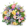 In this image, a beautifully rounded bouquet stands out crisply against a white background, its lush dome of flowers and foliage evoking the refined yet welcoming character of Mill Hill homes. The arrangement is densely filled, every inch covered with petals, berries, and leaves, so that it appears rich and substantial. At the heart are generous garden roses in shades of blush pink, soft yellow, and delicate peach, their petals layered and gently curling, some roses fully open in all their ruffled glory, others just beginning to unfurl. Intertwined with them are airy clematis blossoms, each one a star with fine, tapering petals in tones of white to pale lavender, surrounding vivid yellow or creamy centers that seem to glow softly. Rising up between the more delicate blooms are stems of blue eryngium, or sea holly, their spiky, metallic blue-grey heads and narrow, pointed bracts adding a firm, sculptural quality that hints at wild, open landscapes beyond Mill Hill's parks. Deep purple lisianthus flowers, some still in tight buds, others partially open, nestle among the pastels, bringing a richer hue and velvety texture that deepens the overall palette. Bright red hypericum berries cluster in small bunches, their smooth, round forms catching the light and providing lively bursts of colour that contrast beautifully with the softer tones. The bouquet is cradled in a generous collar of mixed greenery: glossy, broad leaves that anchor the design, finer feathery fronds that soften its outline, and touches of darker, burgundy-tinged foliage that lend subtle drama. Gentle, even lighting enhances the arrangement's textures and round shape, conveying a sense of care, freshness, and quiet celebration, ideal for birthdays, anniversaries, or heartfelt thank-yous delivered across Mill Hill and its surrounding residential streets.