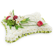A serene, pillow-shaped funeral tribute crafted from a dense carpet of small, pristine white chrysanthemums, photographed against a clean white backdrop so every texture reads clearly. The rectangular cushion surface looks soft to the touch - a tightly packed mosaic of petals that suggests the quiet comfort of a linen pillow - while a pleated band of pale lime-green satin ribbon trims the edges like a gentle frill, catching a trace of soft studio light. On the upper left, a naturalistic cluster rises: two open white Oriental lilies with their pale yellow stamens exposed, a graceful unopened bud, and a scattering of deep burgundy spray carnations whose rich, velvety tones sharpen the composition. Lush green foliage - feathery fern fronds and broader salal-like leaves - forms a verdant backdrop that adds depth and a living contrast against the white chrysanthemum field. From that left cluster a slender, arching loop of natural green grass or decorative wire sweeps across the cushion toward the right, ending in a single deep-red rosebud poised as if in quiet salute, its velvety petals just beginning to unfurl. The overall palette of white, soft lime green, and deep red reads as purity, respect, and enduring affection. This arrangement is composed with classic sympathy language and would be appropriate for a funeral or memorial in Mill Hill - perhaps left near the pulpit at St. Paul's or on a chapel casket at a local funeral home. Available for sensitive local delivery across Mill Hill and Mill Hill Village, it conveys peaceful remembrance and thoughtful care.