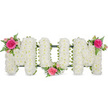 A beautifully arranged floral tribute in the form of the word MUM is captured here against a bright, uncluttered white background, allowing every nuance of petal and leaf to stand out as if viewed in natural daylight. The letters are bold and clearly defined, supported by a hidden dark green frame that provides structure while remaining mostly concealed beneath the flowers. Covering each letter, countless small white spray chrysanthemums have been placed tightly together, creating a soft, padded appearance that feels both comforting and refined. The blossoms are fresh and full, their petals gently curving outwards to form a consistent, cushion-like texture across the entire word. Three carefully positioned accent clusters bring colour and warmth to this serene white base. On the upper left of the first M, a vivid fuchsia garden rose, open at its fullest, takes centre stage, surrounded by pale pink spray roses and buds that introduce a softer tone. Slim, arching fern fronds weave among the roses, their feathery greenery adding lightness and contrast. The central U is gently cradled by a similar floral cluster placed at its lower curve, while the upper right of the second M carries the final matching arrangement, visually balancing the tribute. The whole design looks ready to be placed at a funeral in Mill Hill, perhaps at a local church or crematorium, or laid carefully at a graveside in nearby cemeteries. With its clean whites, tender pinks, and tranquil composition, this MUM tribute offers a heartfelt, traditional way for families in Mill Hill and surrounding North London areas to say a final, loving goodbye to a much-adored mother.