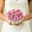 There's an air of gentle promise woven into this artful photograph, where the spirit of Mill Hill seems to bloom anew in every petal. The composition centers on the bride's lightly tanned arms and hands cocooning a symphonic bouquet, its rounded shape brimming with two-tone pink roses hand-selected for their grace by Flowers Mill Hill. Each rose unfurls in a spiral, from pale blush at its heart to a crescendo of magenta lacing the outer petals, imparting a painter's touch of drama. Amidst these, airy sprays of baby's breath are threaded-each cluster evoking a kind of ethereal morning mist, the sort you'd find across the dewy lawns of Mill Hill Park. The bride's nails are immaculately polished in a soft, gentle shade, harmonising with the delicate floral lace that crowns her sleeveless wedding gown. Subtle pearls of a sash tie gather the dress artfully above her hands-a detail both elegant and intimate. The background, all warm, neutral softness, draws the eye back to the radiant flowers and the emotions they evoke. Altogether, this bouquet embodies the optimism, romance, and tradition that echo through Mill Hill's wedding celebrations, capturing in one moment the timeless excitement, careful expertise, and heartfelt meaning placed at the core of every local celebration.