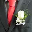 In the soft, cool light the ivory rose at the centre of this boutonnière reads like a small, luminous promise: velvety petals opening in concentric layers, balanced by the froth of baby's breath that gathers at its base like a miniature cloud. Thin, arching sprigs of fern and twisted glossy leaves give the piece a subtle architecture, their dark green curve offering contrast and elegant movement against the matte charcoal of a groom's jacket. A fine white ribbon, tied in a restrained bow, secures the composition and adds a ceremonial whisper without overwhelming the floral simplicity. You can almost sense the tactile coolness of the blooms and the very discreet scent of fresh rose, conjuring early-summer mornings and the hush of a church service or registry ceremony. From a Mill Hill perspective, this boutonnière suits a ceremony at Mill Hill Broadway or a reception at a local village hall, carrying well from photographs on The Ridgeway to a stroll through Mill Hill Park. Prepared with the care you'd expect from a neighbourhood florist, the arrangement is meant to accent, not distract - an understated statement of loyalty and celebration, perfect for a groom, best man, or someone chosen to stand beside the happy couple. For those wanting local convenience, Flowers Mill Hill offers careful handling and same-day assembly to ensure each bloom arrives cool and composed, ready for the day's vows and to be admired in close detail.