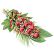 A long, graceful funeral spray is shown resting diagonally across a pure white background, its form gently narrowing from the bound stems at the upper left to the softly fanned greenery at the lower right. The central feature is a line of deep, velvety red roses, each bloom rich with layered petals that range from tightly furled buds to more open blossoms, creating a sense of life unfolding along the length of the arrangement. Between these roses, clusters of small, pinkish-red Hypericum berries are tucked in, their round shapes and slightly lighter colour introducing a delicate texture and soft transition between the roses and greenery. The flowers are supported by an abundant base of dark green foliage: broad, glossy leaves provide a strong, sculpted foundation, while finer leaves and stems give the piece a gentle, organic outline. From the lower right, airy palm fronds extend beyond the main body of the spray, their slender, feathery leaves adding lightness and a flowing, almost cascading feel. At the upper left, the stems are neatly gathered and wrapped in a band of folded green leaf, providing a seamless, natural-looking finish that enhances the formal, respectful tone of the piece. The overall lighting is soft and even, highlighting the contrast between the intense reds, lush greens, and the clean white background. Designed with the quiet charm of Mill Hill in mind, close to local chapels and green spaces like Mill Hill Park, this traditional red rose spray is well suited for funeral services, cremations, or graveside tributes, offering a heartfelt, visually striking expression of sympathy and remembrance for families in the area.