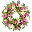 A lavish, round funeral wreath is presented against a crisp white background, giving it the feeling of a floating circle of pink blooms and greenery. The design is compact and abundant, with every inch of the ring covered in flowers and foliage so that the eye moves smoothly around its continuous shape. Deep magenta and vivid fuchsia roses dominate, their velvety petals layered in spirals that create a rich texture across the wreath. Intermixed are softer pink and blush roses, opening more gently to suggest tenderness and fond remembrance. Nestled alongside them, double lilies open wide, with petals in creamy white, blush pink, and soft peach, some showing delicate darker accents toward the edges. A handful of lime-toned lily buds push up between the open flowers, introducing a fresh, living energy to the composition. Surrounding and underpinning the blooms is a thick collar of greenery: fern fronds, with their fine, airy leaflets, soften the outline, while darker, glossy leaves add depth and a polished finish. The overall balance of pinks and greens is both comforting and elegant, heightened by the clean white setting that isolates the wreath, much as a stand would in the quiet of a Mill Hill service hall or crematorium chapel. This is the sort of tribute an experienced local florist like Flowers Mill Hill might prepare for families saying goodbye near Mill Hill East or along Lawrence Street, a wreath designed to speak silently of eternal love, shared memories, and heartfelt sympathy in a time of loss.