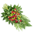The photograph presents a meticulously arranged funeral spray resting on a plain white backdrop, its graceful, tapering shape reminiscent of floral tributes often seen at Mill Hill services and chapels. The design extends diagonally across the image, with a full, rounded head of flowers at the upper left gradually narrowing to a delicate point towards the lower right. At its heart are deep red blooms, led by velvety roses whose petals curl in rich, spiralled layers, joined by bold red gerbera daisies with dark, expressive centres and clusters of ruffled red carnations. Together, they create a warm and dignified palette that suggests love, respect, and cherished memories. Threaded between these crimson flowers are bright lime-green chrysanthemum pompons, compact and spherical, their luminous green tone introducing a modern, uplifting contrast. Scattered sprigs of tiny white filler flowers, perhaps gypsophila or small daisies, soften the stronger colours and add gentle, cloud-like touches of light. Surrounding the blooms is an abundant frame of greenery: broad, glossy dark green leaves provide structure and depth, while feathery fern fronds and other verdant textures extend the outline of the spray in all directions. To the lower right, long, slim leaves are fanned outward in a smooth arc, underscoring the arrangement's elegant flow. At the top left, a cluster of upright stems or leaves is gathered, with one broad leaf wrapped around them to create a neat, sculptural accent. The finished piece feels composed and serene, a fitting floral tribute for a funeral in Mill Hill, whether placed near Mill Hill Park, in a local church, or within a quiet family gathering space along the surrounding residential roads.